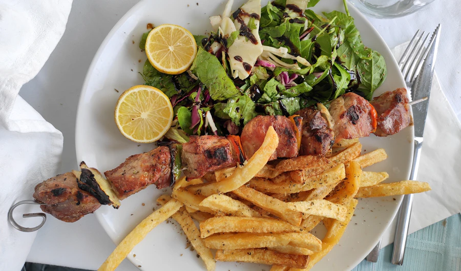 Plate of souvlaki skewers with fries, salad and lemon